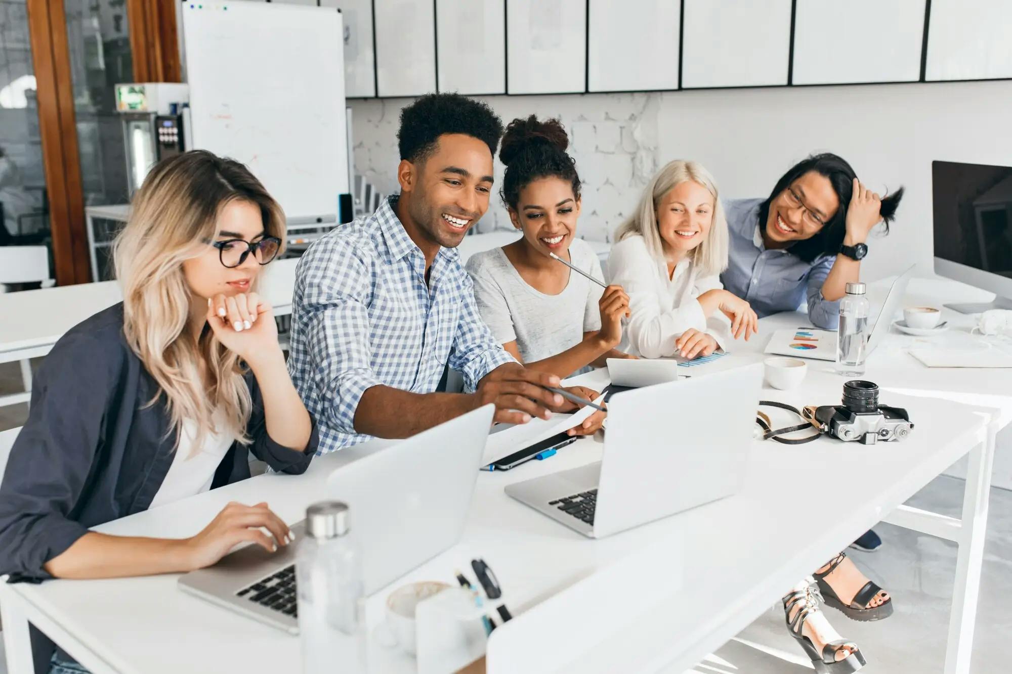 Diverse group of students smiling and collaborating on laptops around a desk